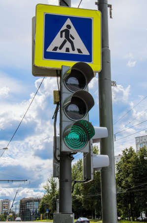 Traffic light with a burning green signal and a pedestrian crossing sign against the blue sky. Traffic safety, urban traffic regulation. Vertical image.の写真素材