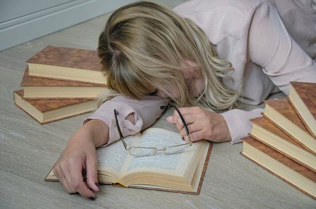 Young blonde woman is surrounded by books had fallen asleep on the floor while studying. Glasses on...