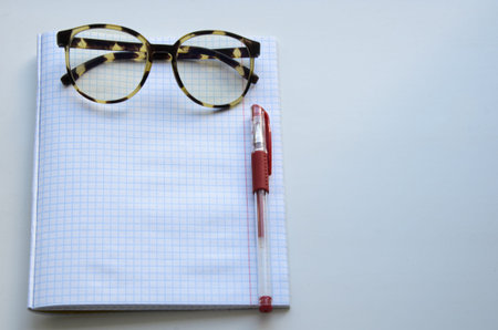 Horn-rimmed glasses, red ink pen on a checkered notebook. The concept of learning, student body,...