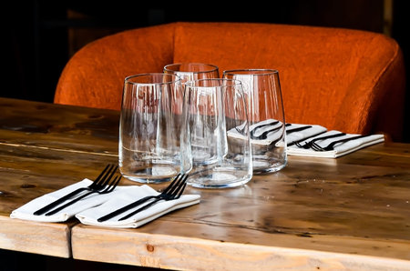 Table on restaurant, served for four: glasses, napkins and cutlery on wooden table and the orange...