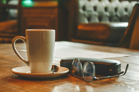 Tall white coffee mug with glasses and a case from glasses on a wooden table in a cafe. The concept...