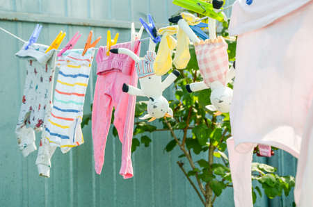 Washed colorful clothes for children and stuffed animal goats, are dried on a rope on clothespins outside. Laundry and housework, childcare, life in a country house.の写真素材