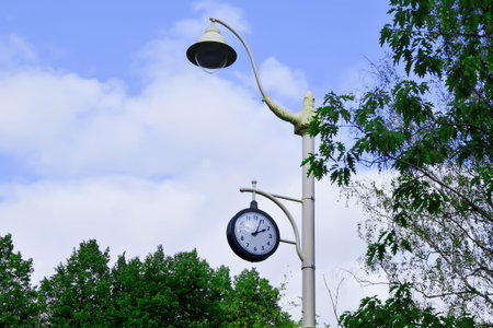 City lamppost with a modern lamp and round street clock showing 02:05 pm, against blue sky...