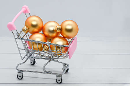 Metal supermarket trolley full of Christmas balls on white background. Christmas sales symbol, buying gifts, preparing for the holidays. Space for text on the right.の写真素材