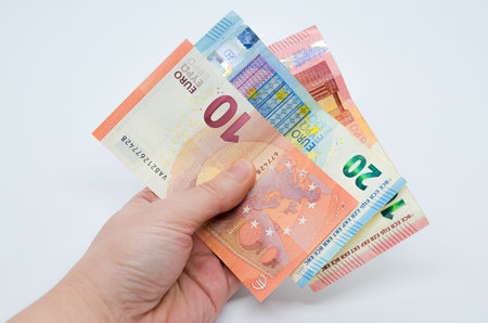 Hand holds paper bills of Euro currency in denominations of 10 and 20 on white background. Money...