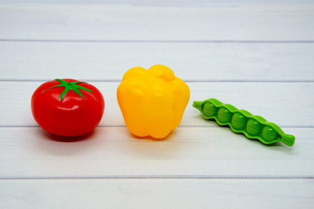 Toy plastic vegetables: tomato, bell pepper, green peas on light wooden tabletop. Vegetables...