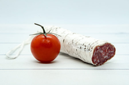 Close-up French and Catalonia Fuet cured pork sausage with slices and cherry tomato on light wooden...