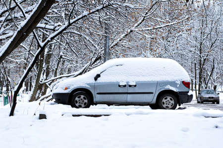 Car in city parking under snow after snowfall in winter day surrounded by snowy trees. Moscow Russia - 11.23.2020のeditorial素材