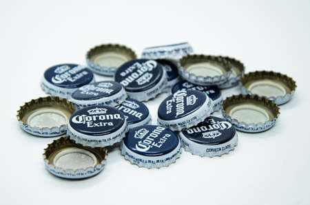 Pile of scattered caps from beer Corona Extra produced by Cerveceria Modelo in Mexico on white background. Concept: end of holiday, after party, symbol. Moscow Russia - 11.26.2020のeditorial素材