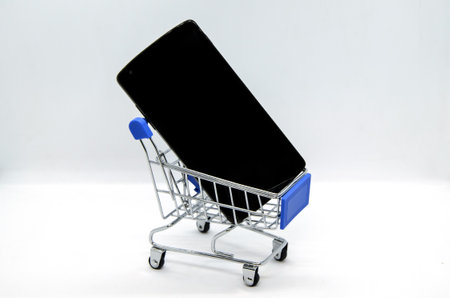 Metal supermarket trolley with smartphone on white background. Concept: online shopping, delivery of online orders, buying and selling goods using smartphone, supermarket application.の写真素材