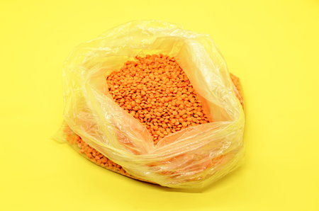 Red lentils in a transparent plastic bag on a yellow background. Traditional cereals, food...