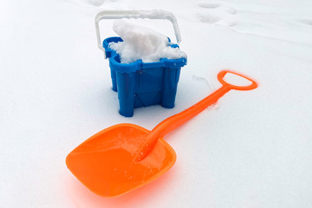Children's snow shovel and bucket filled with snow on snowy area. Winter outdoor activities, accessories for children's educational games with snow. Winter activitiesの写真素材