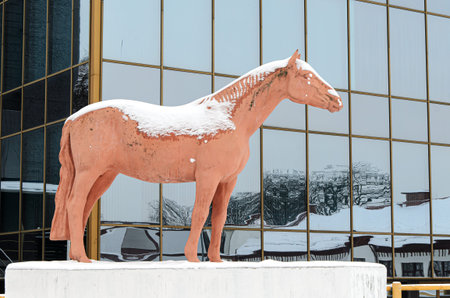 Snow-covered sculpture of horse in city park against backdrop of a glass facade of high-rise building with reflections of other houses. Symbol of animal husbandry at VDNKh. Moscow Russia 07-01-2021のeditorial素材