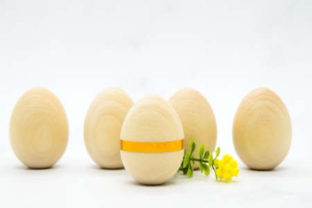 Wooden eggs with a gold ribbon and yellow flower on light marble background. Space for text. Postcard, banner for congratulations with Easter. Minimalistic Easter background in light colors.の写真素材