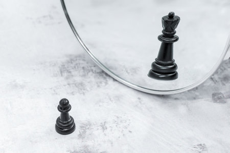 Black chess pawn in front of mirror sees reflection of chess queen. The concept of career growth, transformation. Proverb illustration: soldier who doesn't want to be general is bad soldierの写真素材