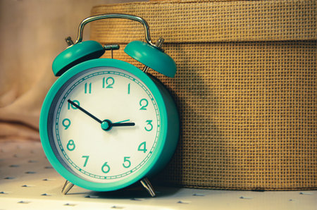 Vintage image of old alarm clock on background of wicker straw hat box. Interior decorative...