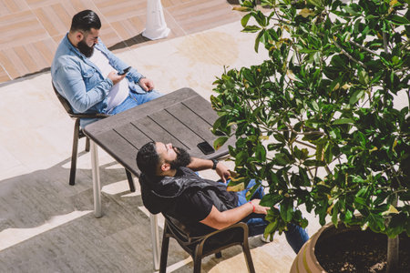 Evrenseki, Turkey - 03.18.2021 Two black-haired men with beards sit at a table in a street cafe and...