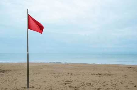 Empty sandy beach and red storm flag on a cloudy day. Security on public and private beaches, storm alert system.の写真素材