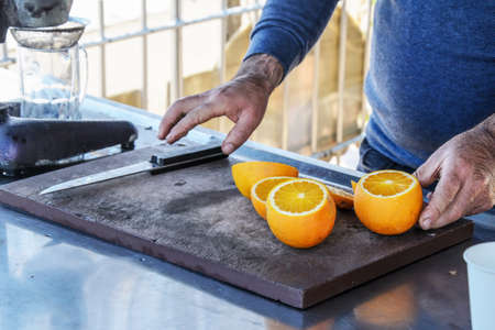 Male hairy hands make freshly squeezed orange juice at a beach cafe by the sea. High season tourist service, seaside restaurant.の写真素材