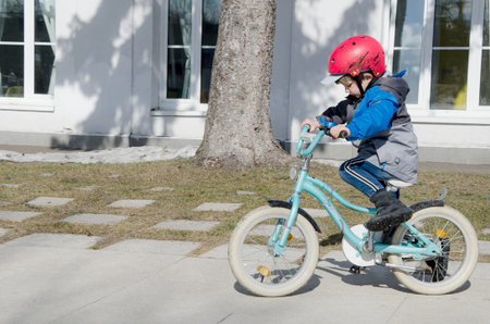 Moscow, Russia 03.28.2021 - Little boy in red safety helmet in demi jacket learning to ride a two-wheeled bike. Activities with children in the park.のeditorial素材