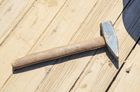 Metal hammer with wooden handle on dirty boards in sunlight. Hand construction tools, repair