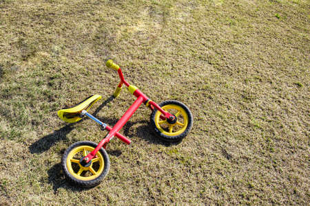 Children's balance bike with a red frame lies on the spring lawn in the park. Active holidays with the whole family. Sports equipment for children. Copyspaceの写真素材
