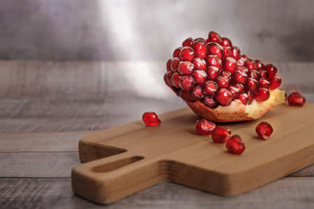 Close-up of peeled pomegranate wedges and pomegranate seeds on a wooden board in sunlight. Dark vintage rustic background.の写真素材