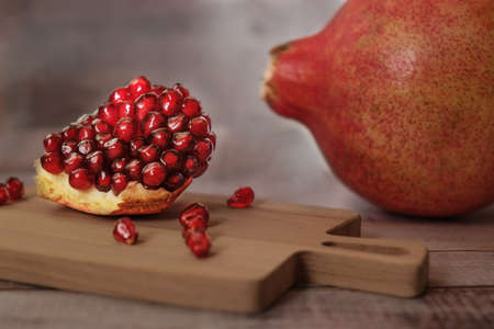 Close-up of peeled pomegranate wedges and pomegranate seeds on a wooden board in sunlight. In the background there is a whole large unpeeled pomegranate. Dark vintage rustic background.の写真素材