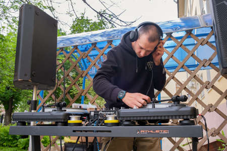 Young man in a sweatshirt stands behind the DJ console with the headphones on his head. DJ mixes music at the console during a music set in a trendy youth bar.のeditorial素材