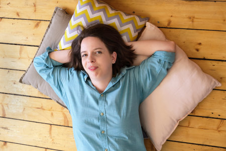 Young brunette woman with shoulder-length hair lies on pillows her head resting on her hands. Woman...