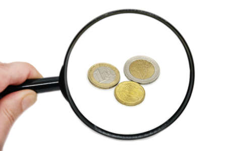 Euro coins magnified in a hand-held magnifier on a white background. A man holds a magnifying glass over coins. Inflation, poverty, economic crisis concept.の写真素材