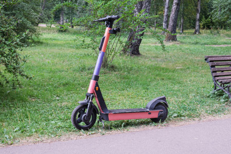 Abandoned electric scooter near the path in a city park. Discharged electric scooter battery. City...