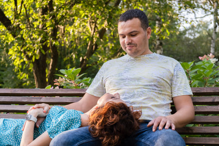 Loving couple on a park bench look at each other with tenderness. The wife lies on her husband's...
