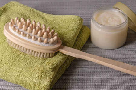 Double-sided massage brush for body brushing lies on towel on background body scrub. Pins of natural wood for removing of cellulite and stimulating your lymphatic system. Materials for spa treatmentsの写真素材