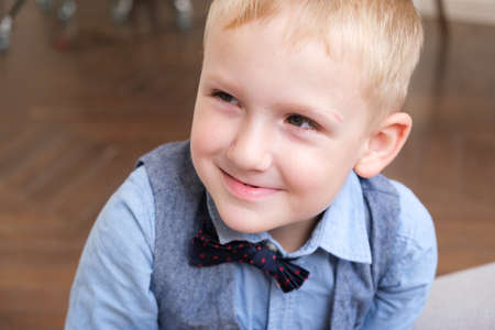Portrait of a five-year-old blonde boy in a shirt, vest and bow tie. Close-up of the child's face. The boy smiles and squints.の写真素材