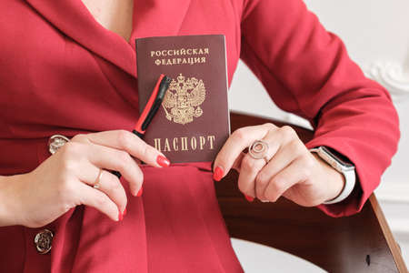 Passport of a citizen of the Russian Federation in the hands of a woman. The hands of a woman in a red dress hold a Russian passport and a pen.の写真素材