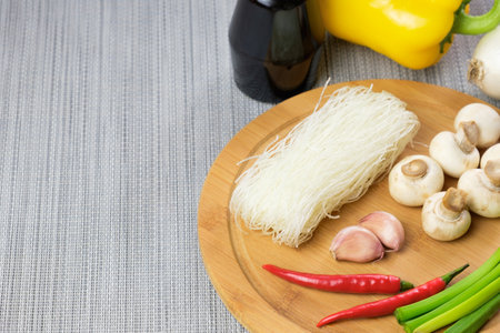 Dry funchose glass Chinese noodles and ingredients for preparing an Asian dish. Glass noodles, champignons, hot pepper pods, green onions, garlic, soy sauce on cutting board. Top view, space for textの写真素材