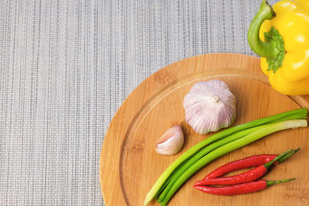 Vegetables on wooden cutting board for cooking. Sweet yellow peppers, hot chili peppers, garlic, green onions are on table. Seasonings to add tangy flavor to food. Culinary template for adding text.の写真素材