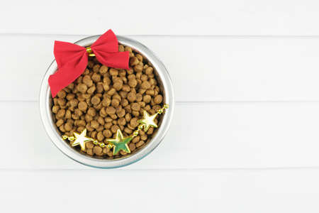 Metal bowl with dry pet food and Christmas decorations on light boards. Christmas pet supplies concept, New year and Christmas celebration. Top view, space to insert text.の写真素材