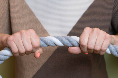 Female hands hold a thick twisted rope. A horizontally stretched rope in the hands of a woman. A symbol of struggle, a metaphor for overcoming difficulties, a strong bondの写真素材