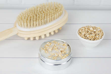 Means for the production of natural scrub from body cream and oatmeal. Delicate cleansing of the skin of the body - wooden massage anti-cellulite brush and jar of oatmeal purifying maskの写真素材