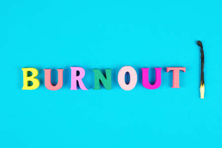 Word burnout from multicolored wooden letters and burnt match on blue background. Burnout metaphor. State of emotional, physical, and mental exhaustion caused by excessive and prolonged stressの写真素材