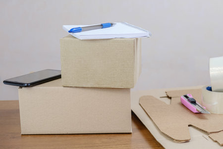Cardboard boxes with packed orders of online store are on table in warehouse. Smartphone and...