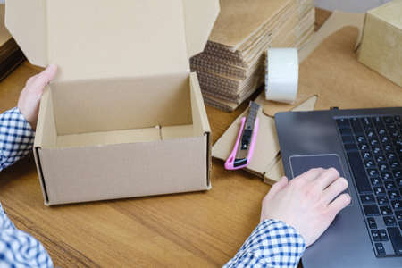 Woman at the desk packs an order from an online store in a cardboard box. Warehouse employee processes and packs order for delivery, warehouse goods logistics. Small business, work from homeの写真素材