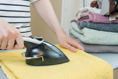 Woman strokes a clean yellow terry towel with an iron. Woman at the ironing board. Housework, ironing.の写真素材