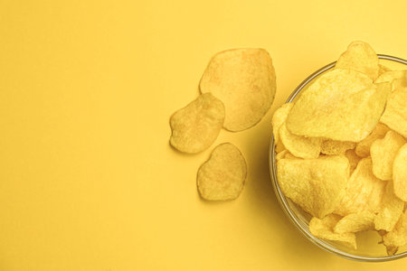 Potato chips in a round bowl on a yellow background. Space for text on the left. top view. The most popular snack. junk food.の写真素材