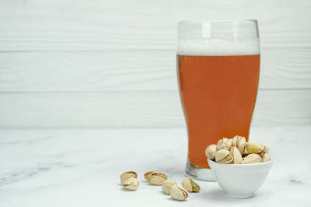 Glass of beer and a popular snack - fried salted pistachios. Space for text.の写真素材