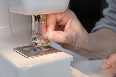 Seamstress threads a needle on an electric sewing machine. Close-up of hands. tailor workflow...