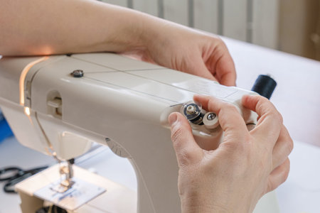 Seamstress winds thread on the bobbin of an electric sewing machine. Close-up of hands. tailor...