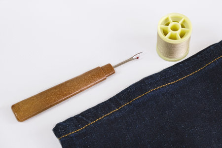 Close-up of seam ripper, spool of thread and stitched denim. Seamstress tools, mending clothes,...